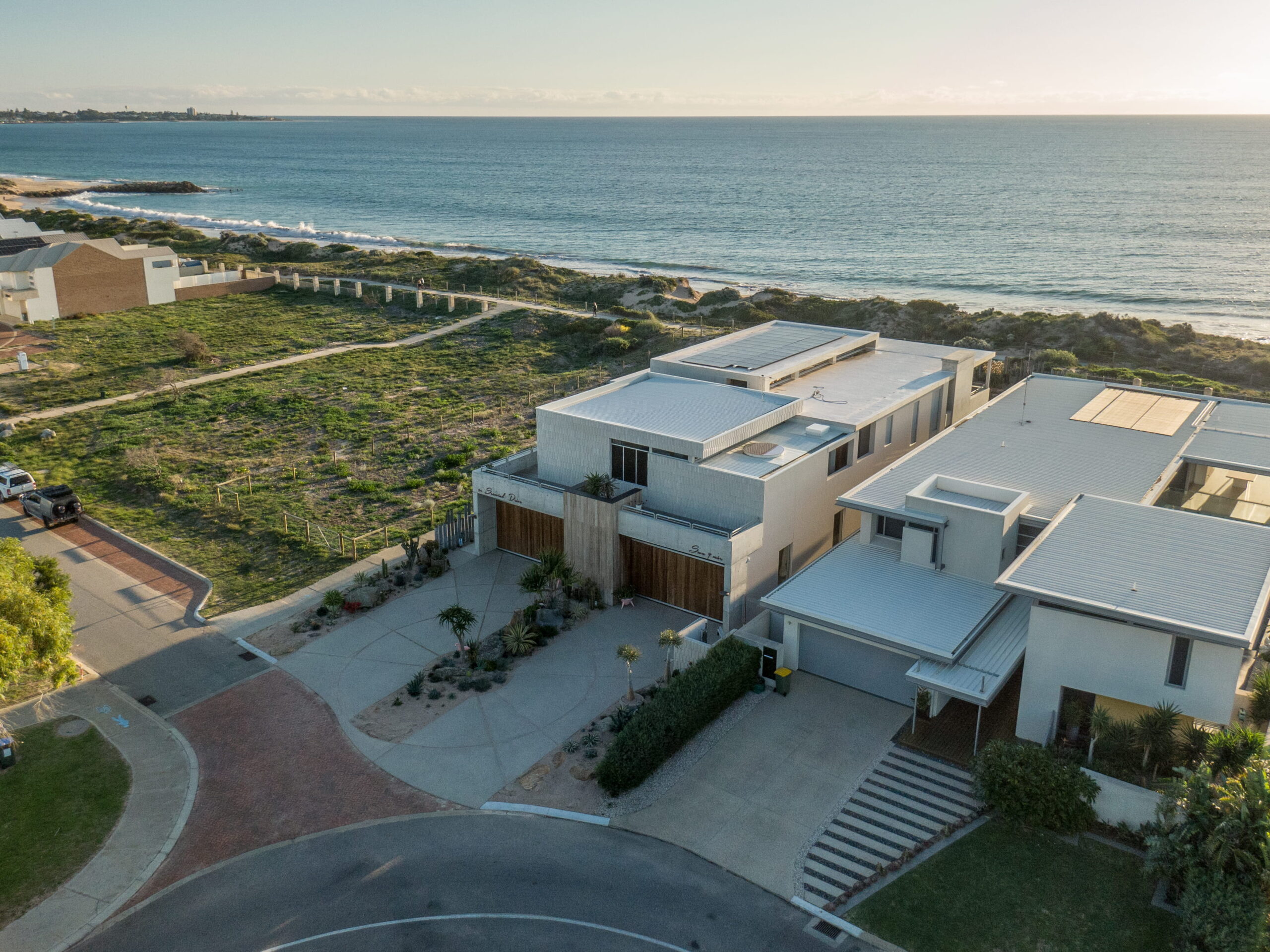 Aerial View of Two Luxury Multi-story Coastal Homes with Solar Panels and Native Landscaping on a Beachfront Road.