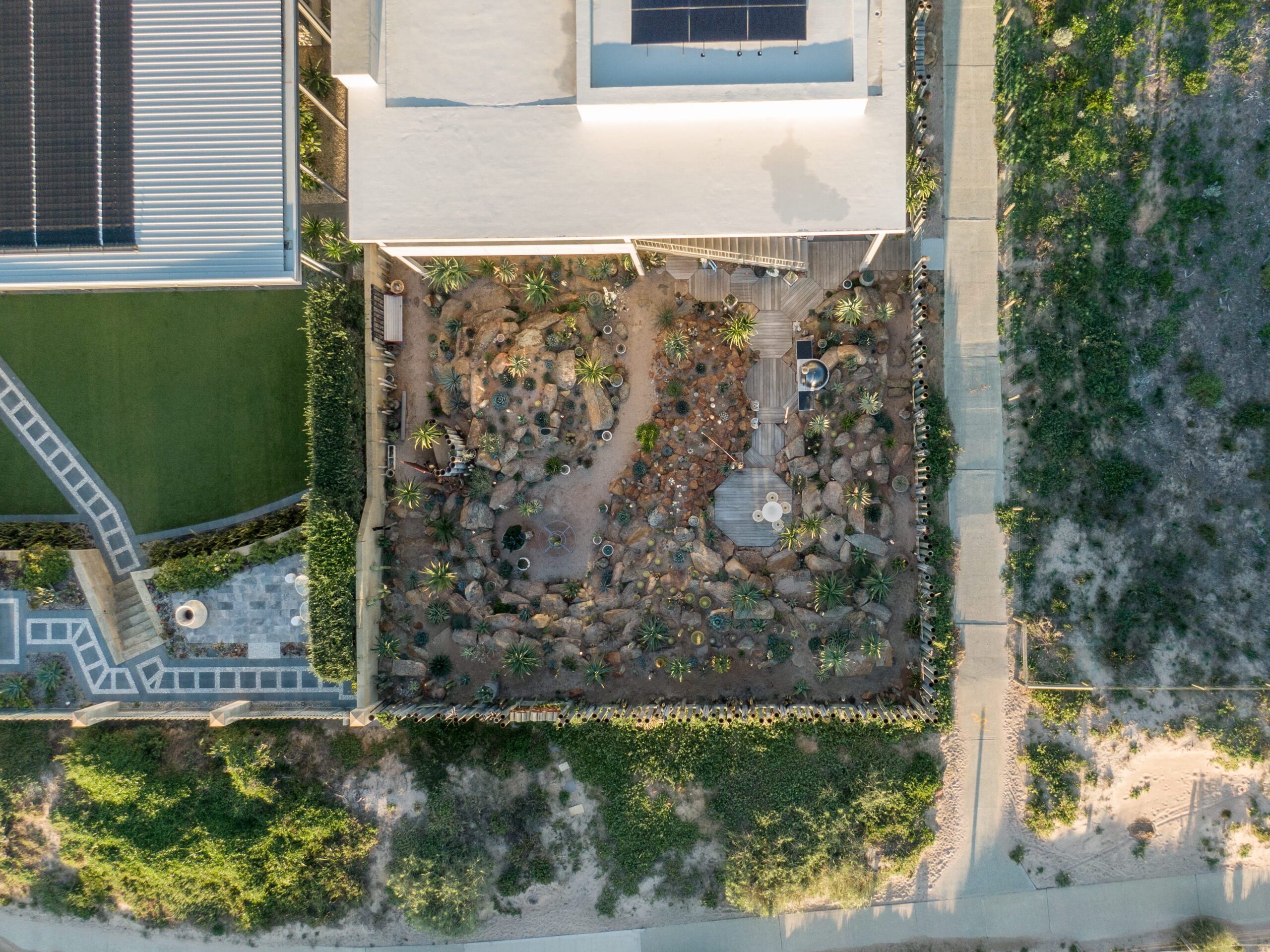 Top-down Aerial View of a Coastal Home's Rock and Plant Landscaping Situated Directly Next to Sandy Coastal Dunes.