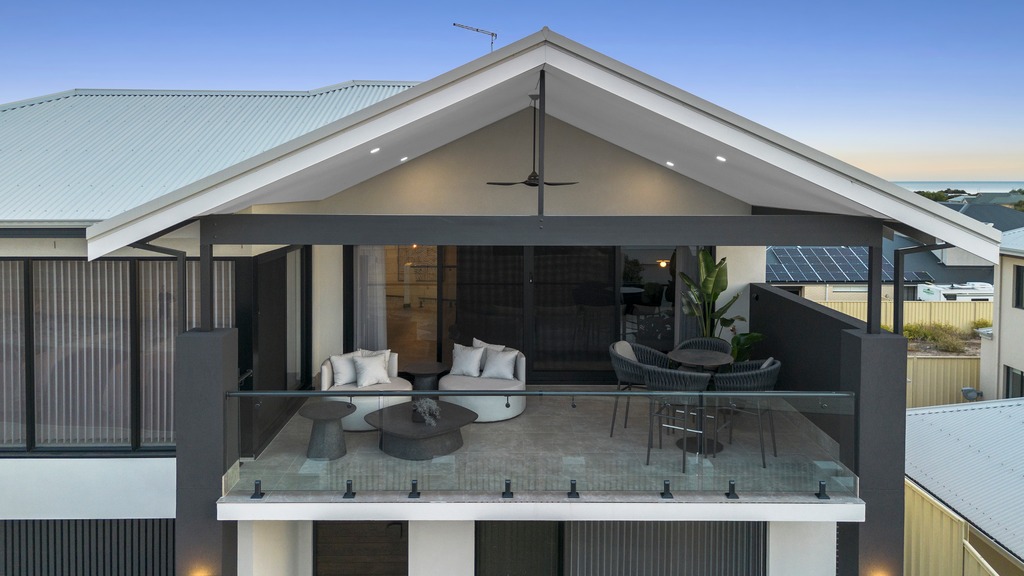Contemporary upper-floor alfresco balcony with frameless glass balustrade and outdoor lounge seating.