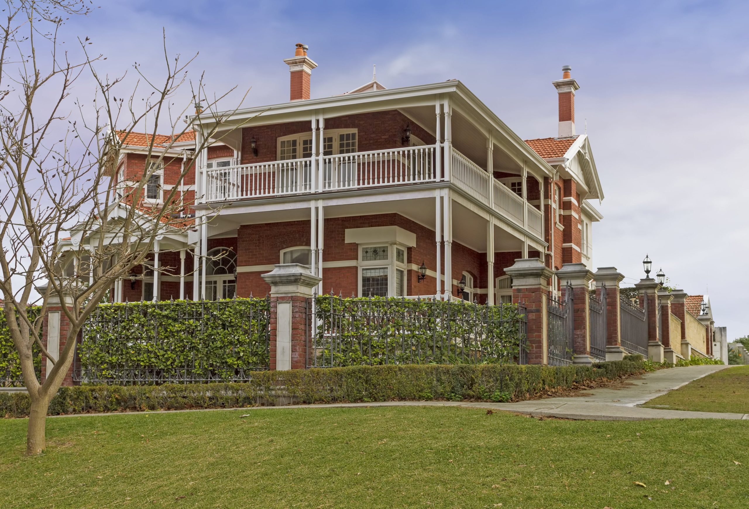 Traditional luxury brick home with wraparound upper-floor balcony and heritage architectural detailing.