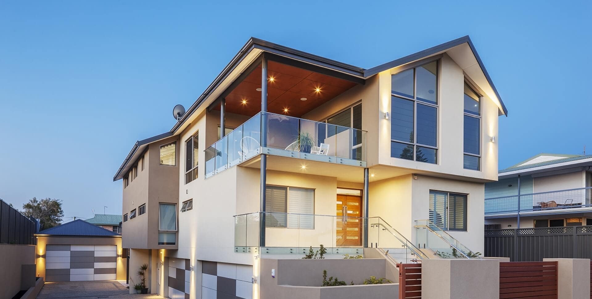 Modern double-storey coastal home with frameless glass balcony and contemporary exterior lighting